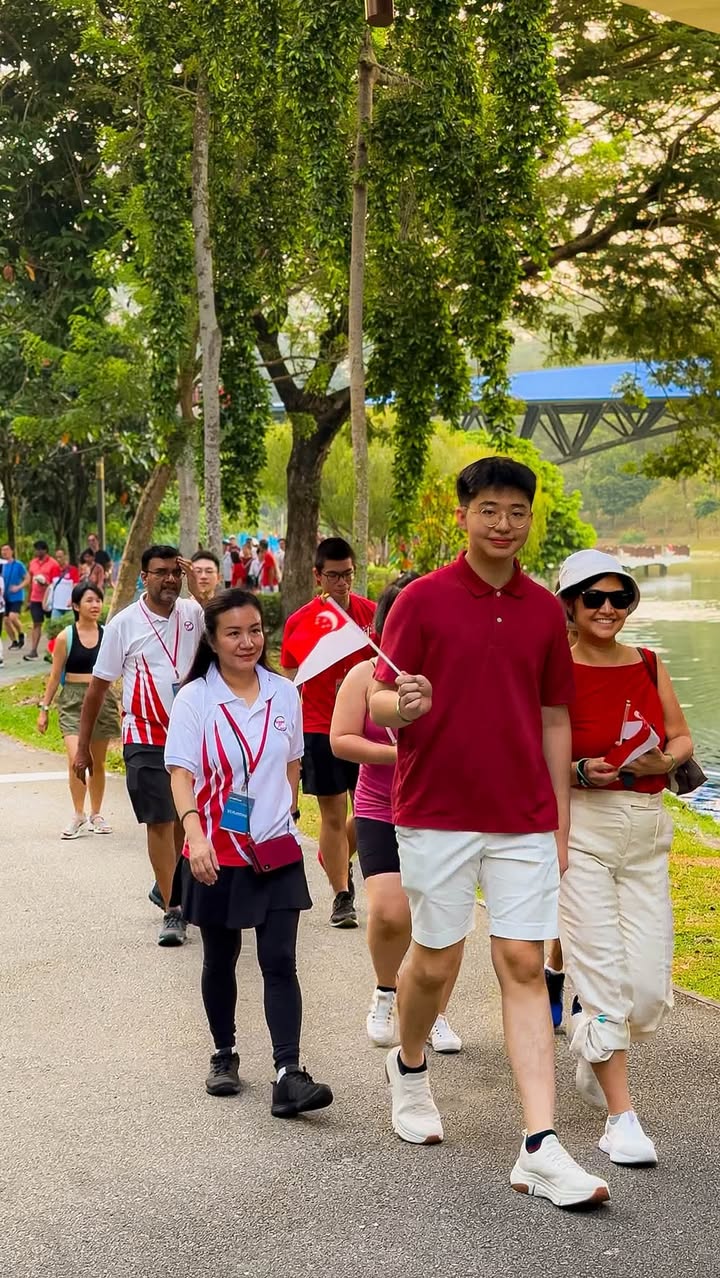 Participants walking outdoors holding Singapore flags near a waterway