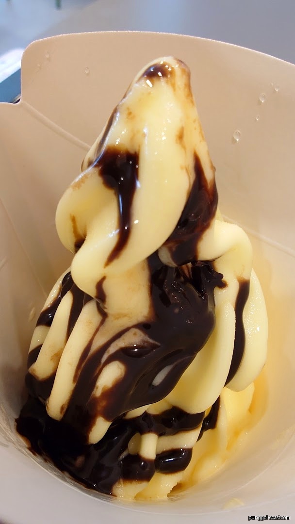 Close-up of soft-serve ice cream with chocolate syrup in a white cup.