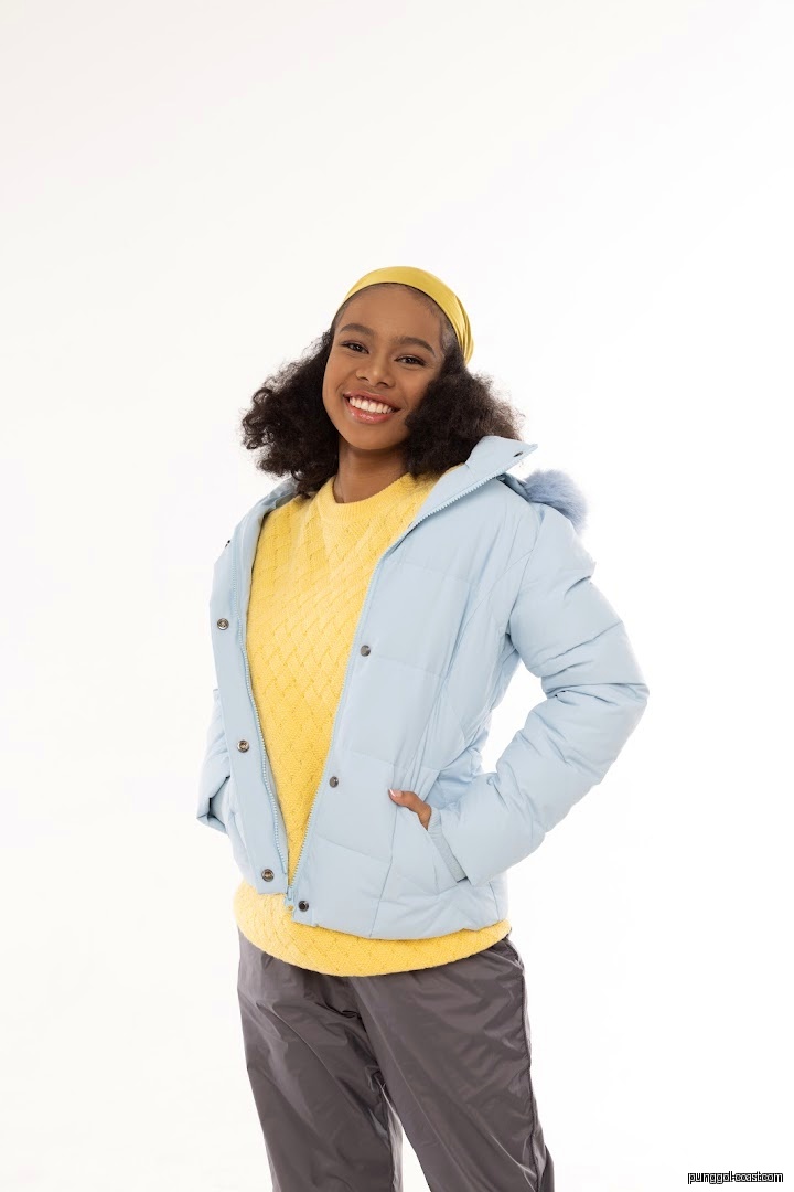 Smiling person wearing light blue puffer jacket and yellow sweater.