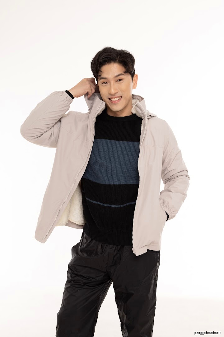 Smiling male model wearing a light jacket, striped sweater, and black pants.