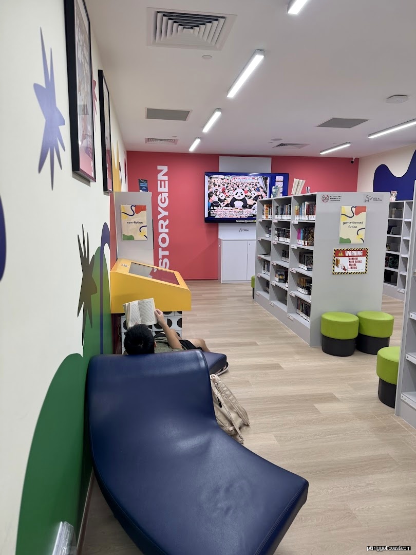 Interior view of a library showing bookshelves, seating, and a person reading.