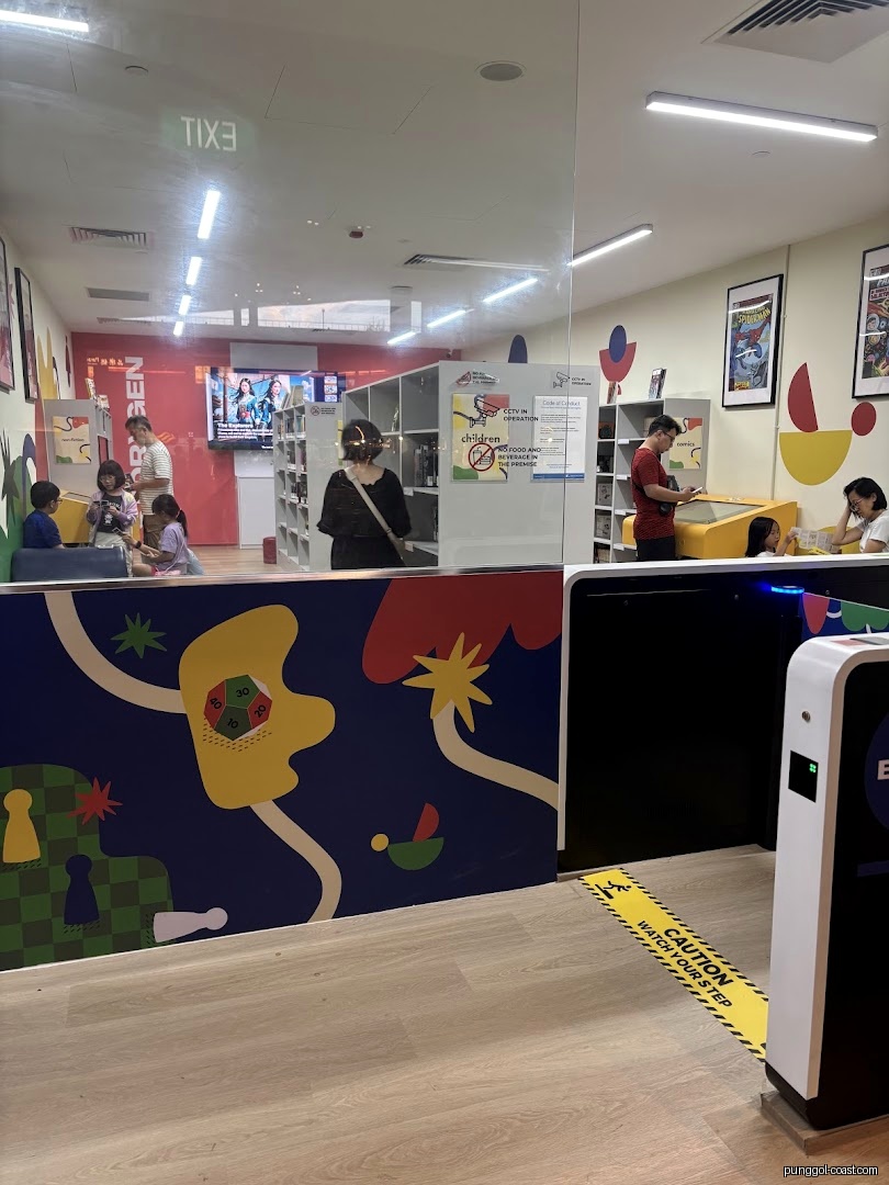 Interior view of a library/shop with people, shelves, and colorful decor.
