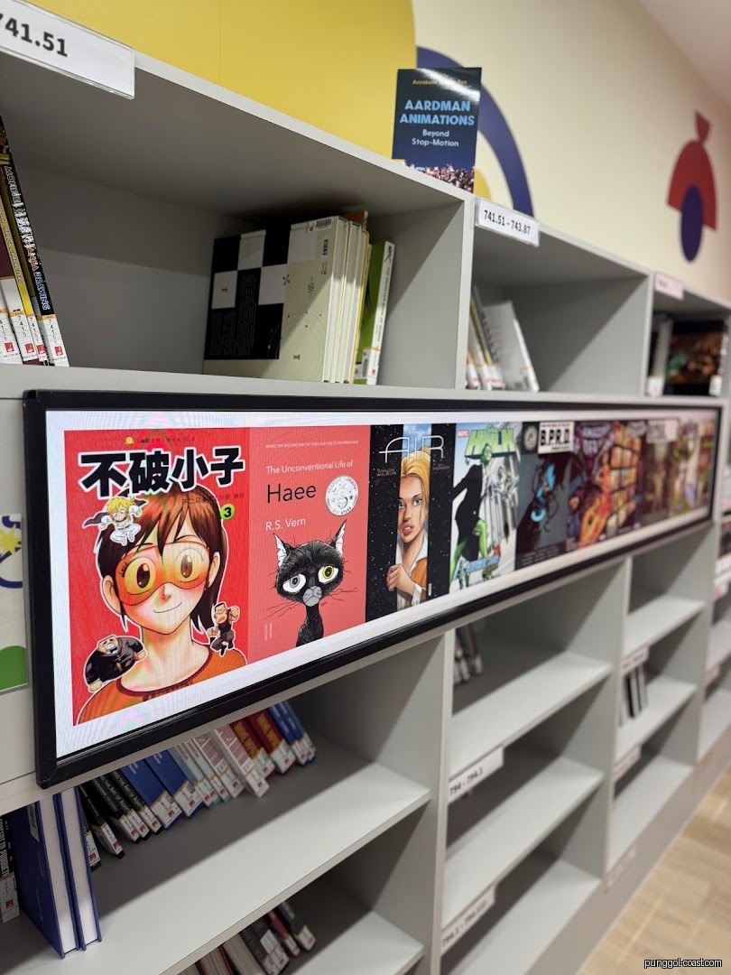Shelves of comics and books with a digital display in a library setting.