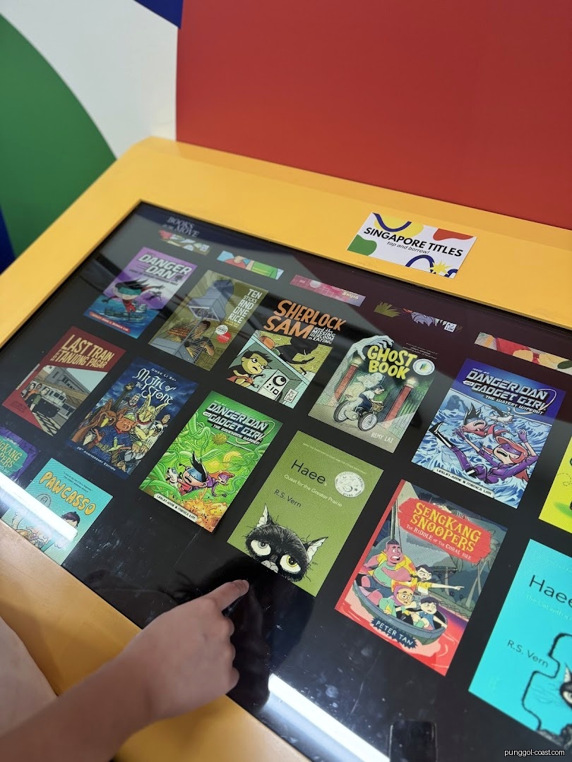Hand interacting with an interactive display table showing various book covers.