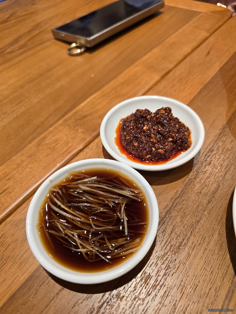 Two condiment bowls with chili and soy sauce on a wooden table.