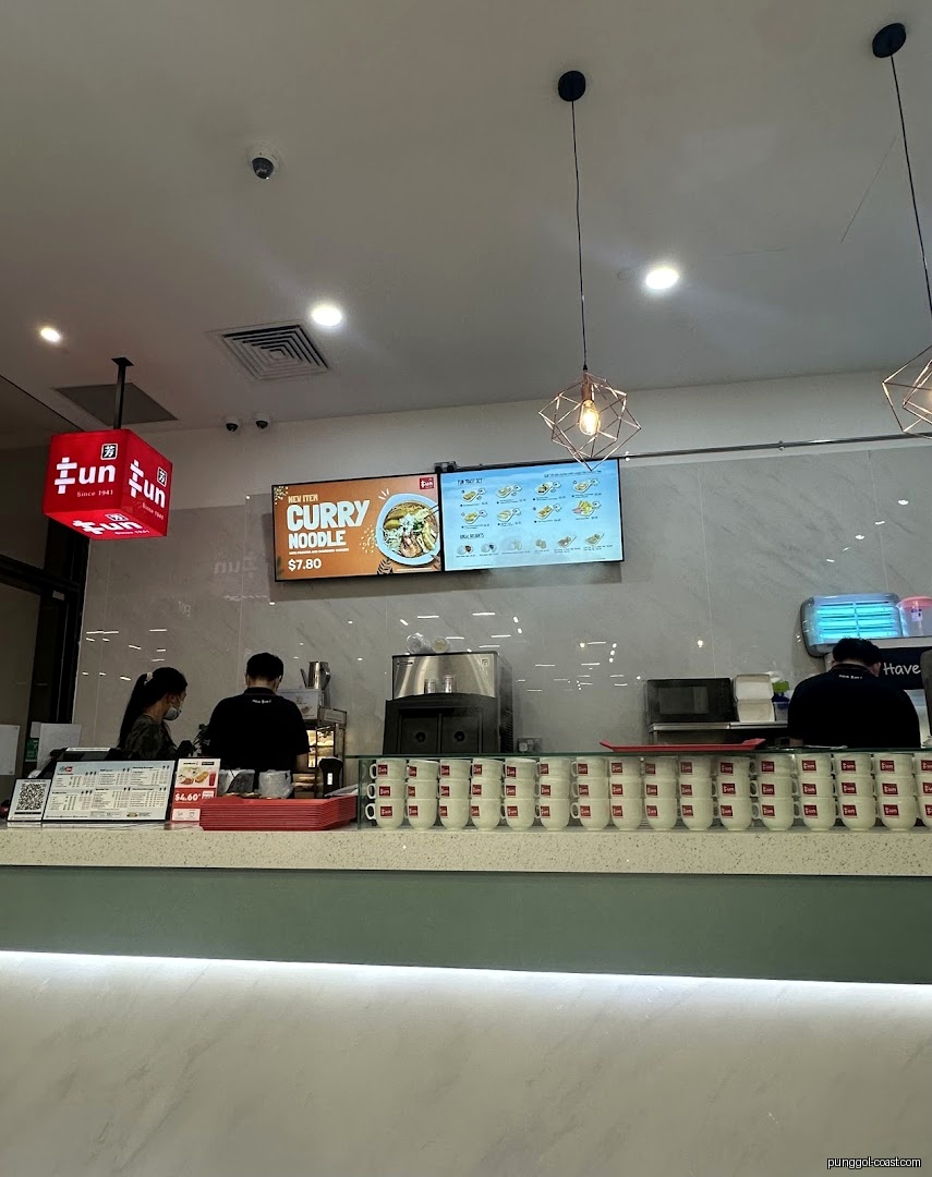 Interior view of a food counter with staff, digital menus, and stacked cups.