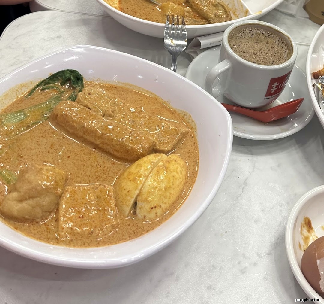 Close-up of a bowl of curry with tofu and eggs, and a coffee cup.