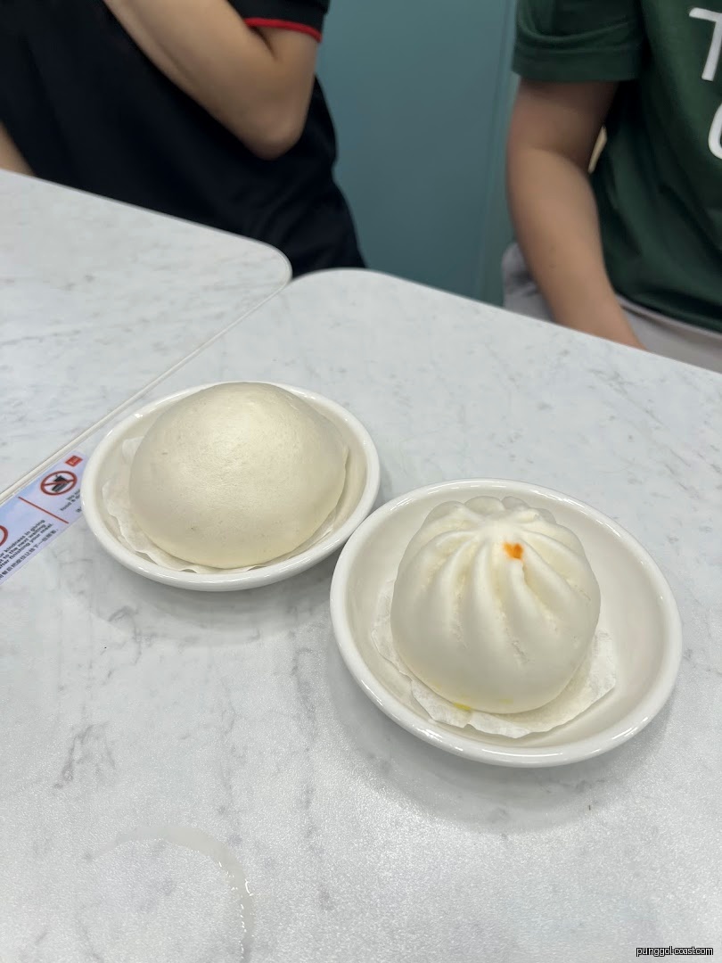 Two steamed buns on white plates on a marble-patterned table.