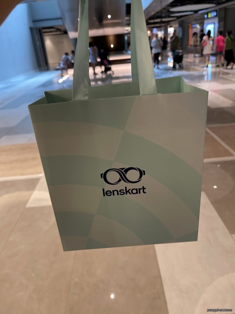 A Lenskart shopping bag held in a mall setting.