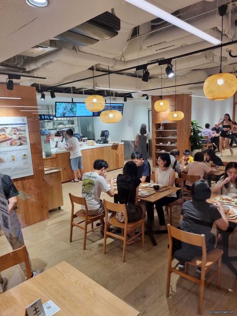 People are dining inside a bright, modern cafe with wooden furniture.