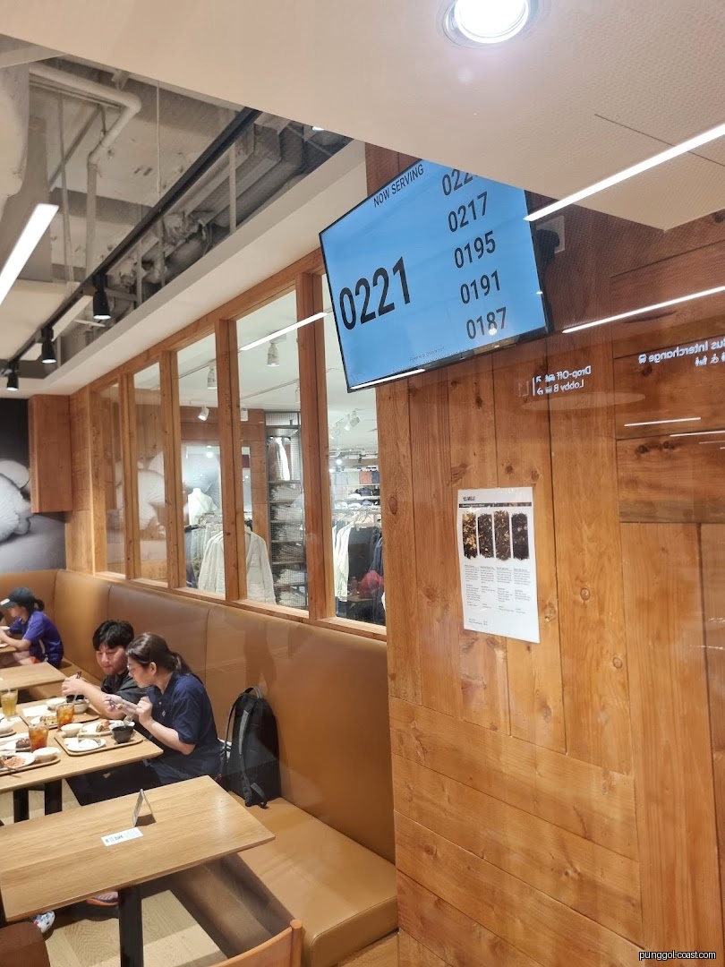 Customers dine in a cafe setting with a queue screen and retail view.