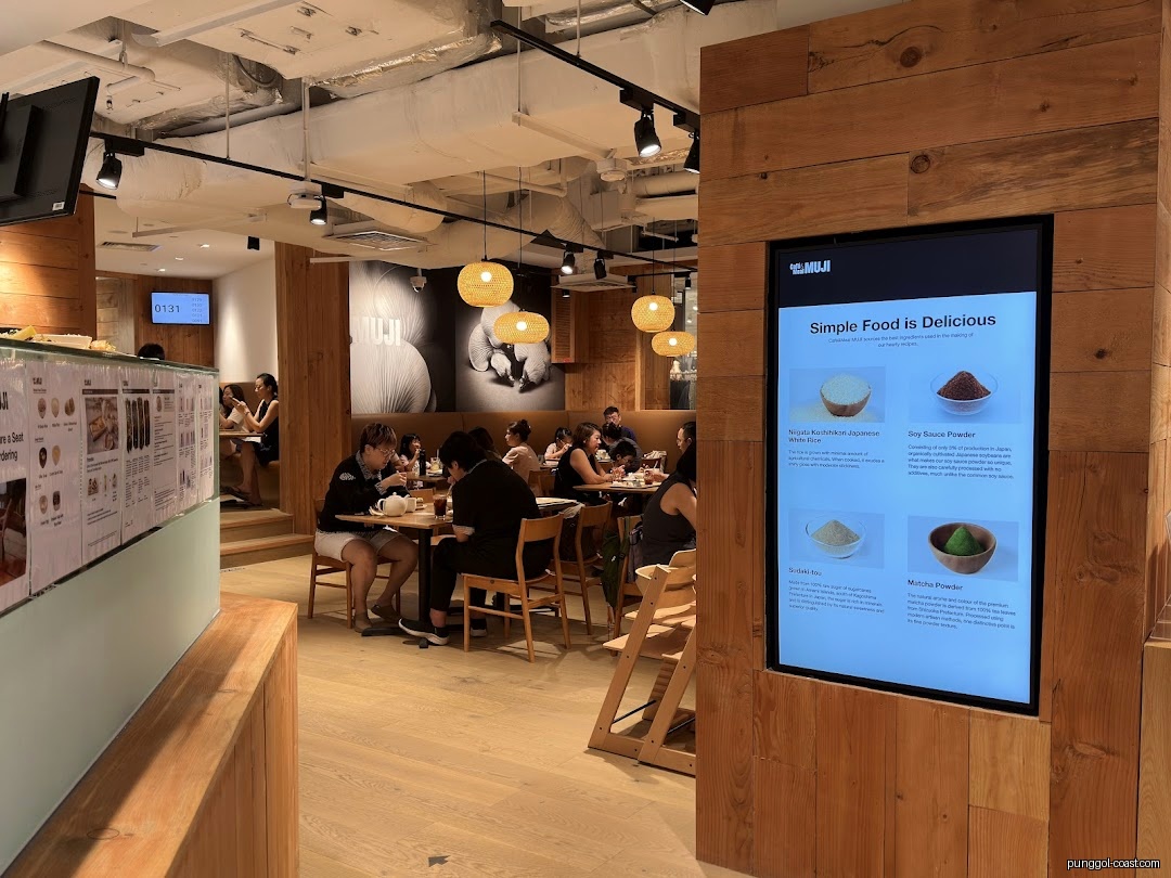 People are dining in a modern Muji cafe interior with a digital food display.