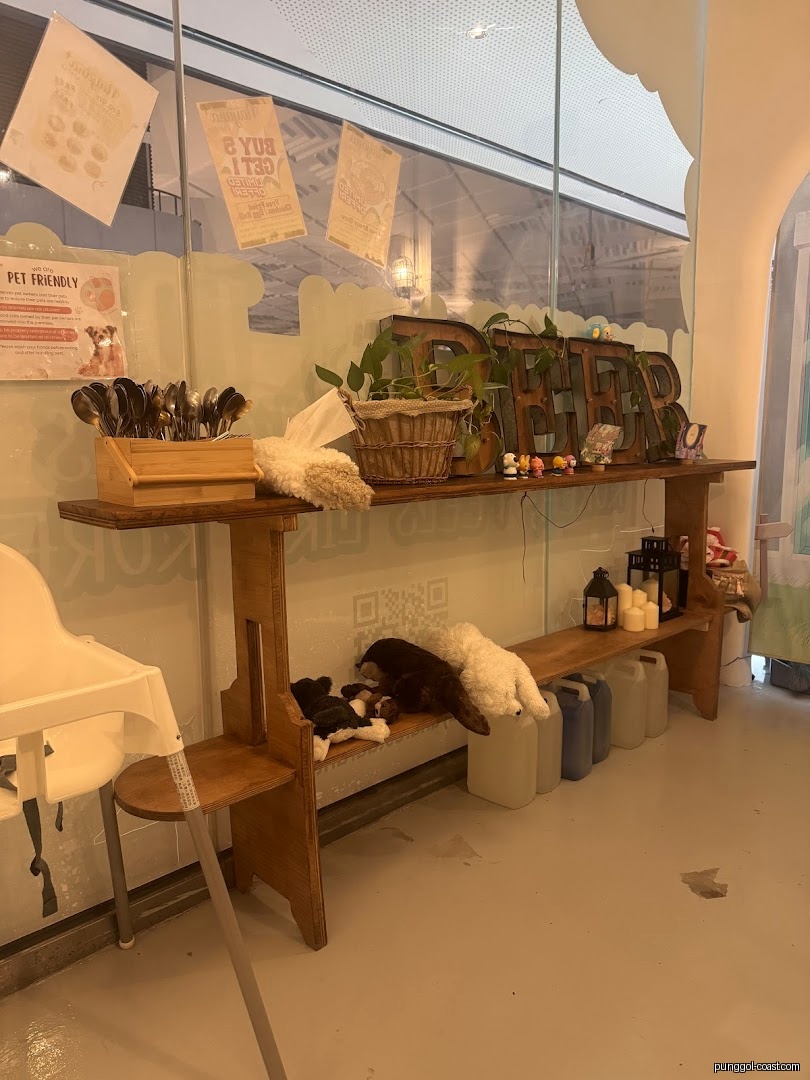 Decorated wooden shelf with utensils, plants, and stuffed animals inside a cafe.