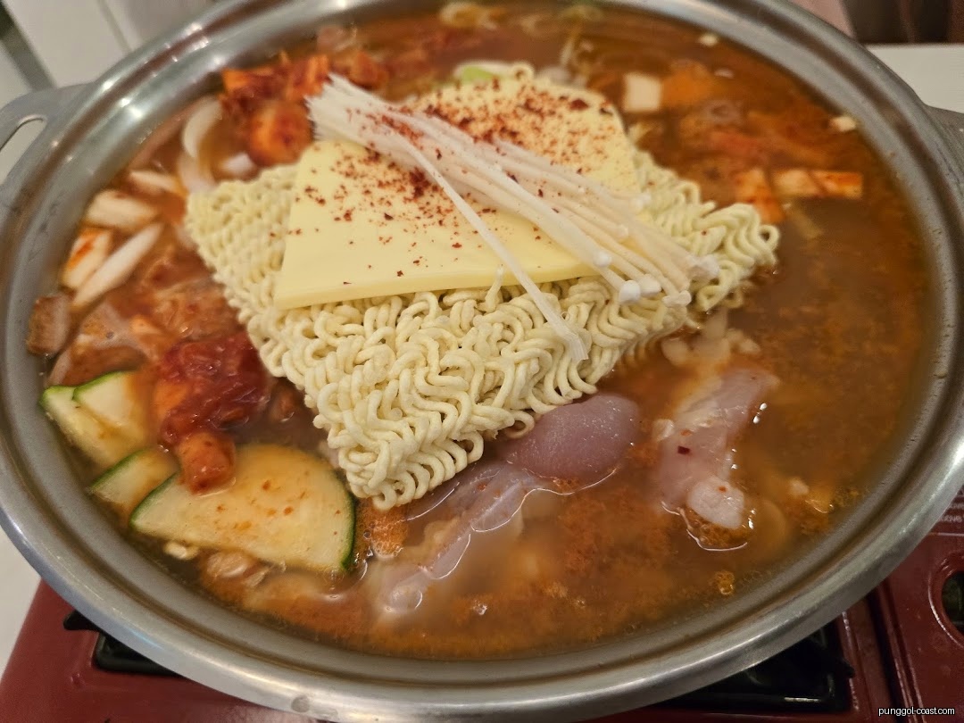 Close-up of a hot pot with ramen noodles, cheese, and vegetables.