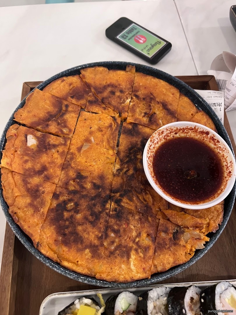 Kimchi pancake with sauce and sushi rolls on a table.