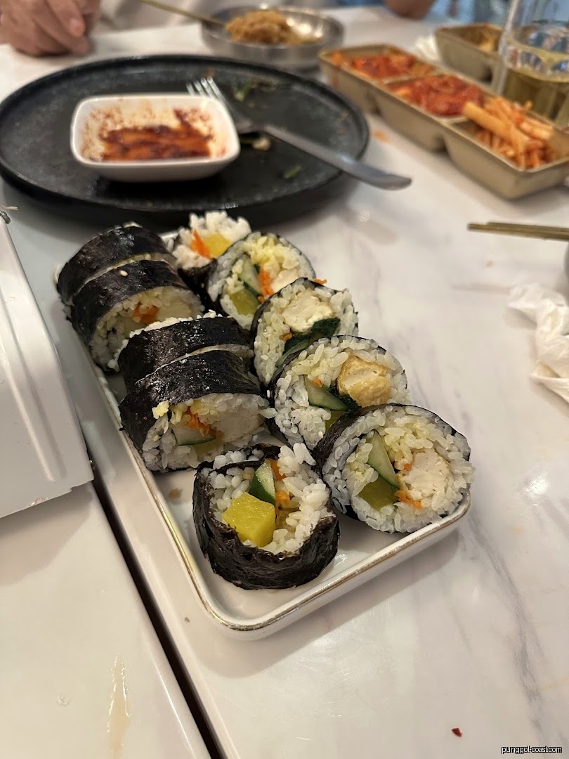 A plate of gimbap on a table with other dishes and a dipping sauce.