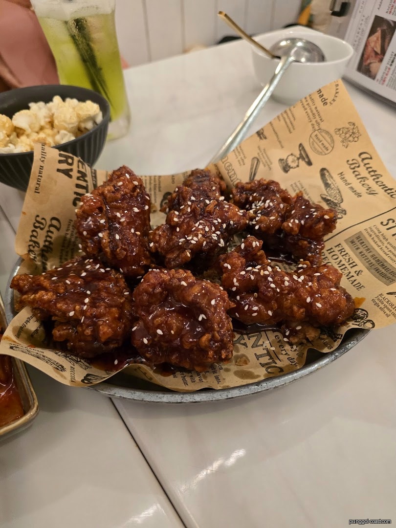 A plate of sauced fried chicken with sesame seeds on a table.