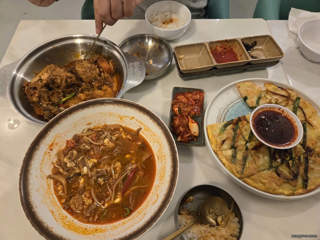 Table with multiple Korean dishes, including stews, pancakes, and kimchi.