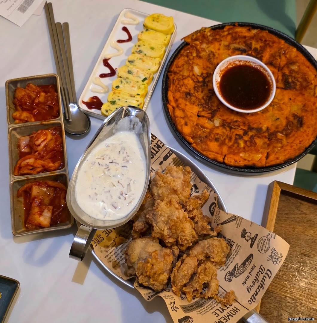 Table with various Korean dishes: fried chicken, pancake, egg rolls, and kimchi.