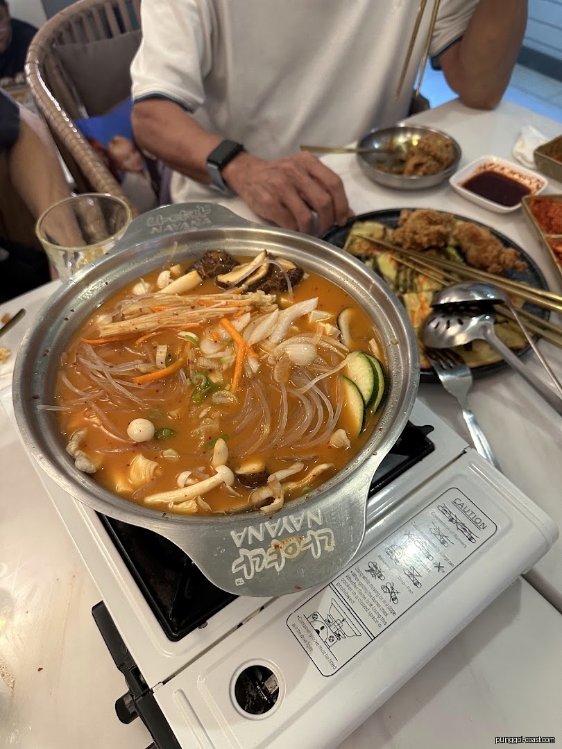 Close-up of a hot pot with noodles and vegetables on a table.