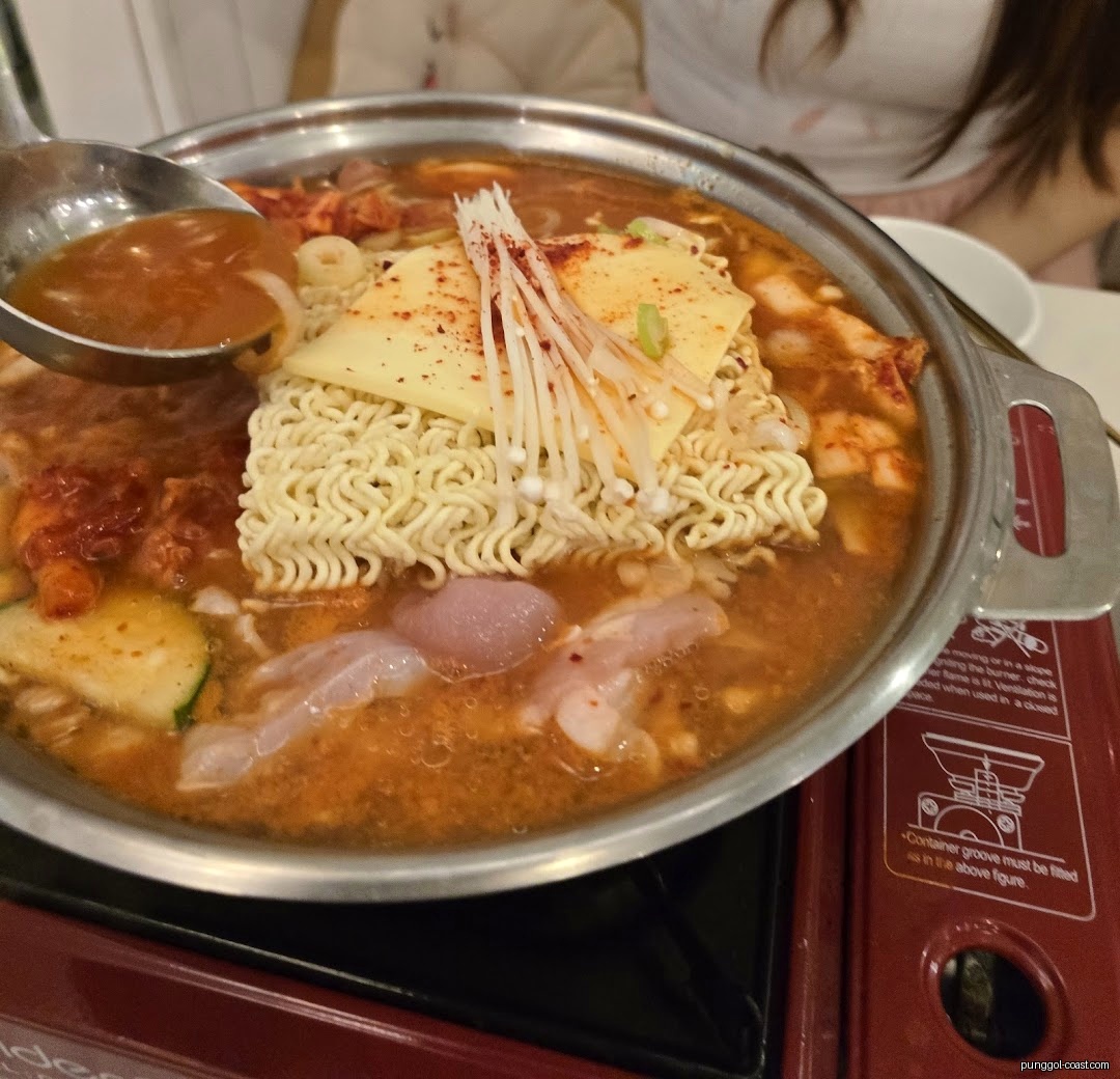 Close-up of a bubbling Korean hot pot with noodles, cheese, and mushrooms.