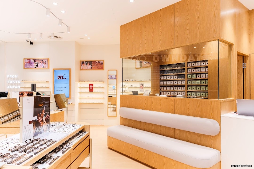 Interior view of an optical shop with eyeglasses displays, wooden furnishings, and a waiting bench.