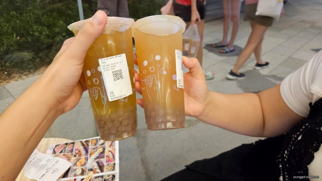 Two hands holding two large grape tea drinks with pearls.
