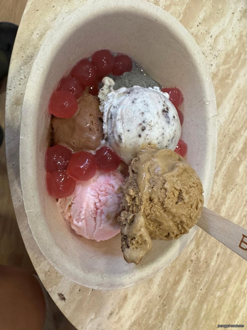 A bowl of various ice cream scoops with red boba pearls and a wooden spoon.