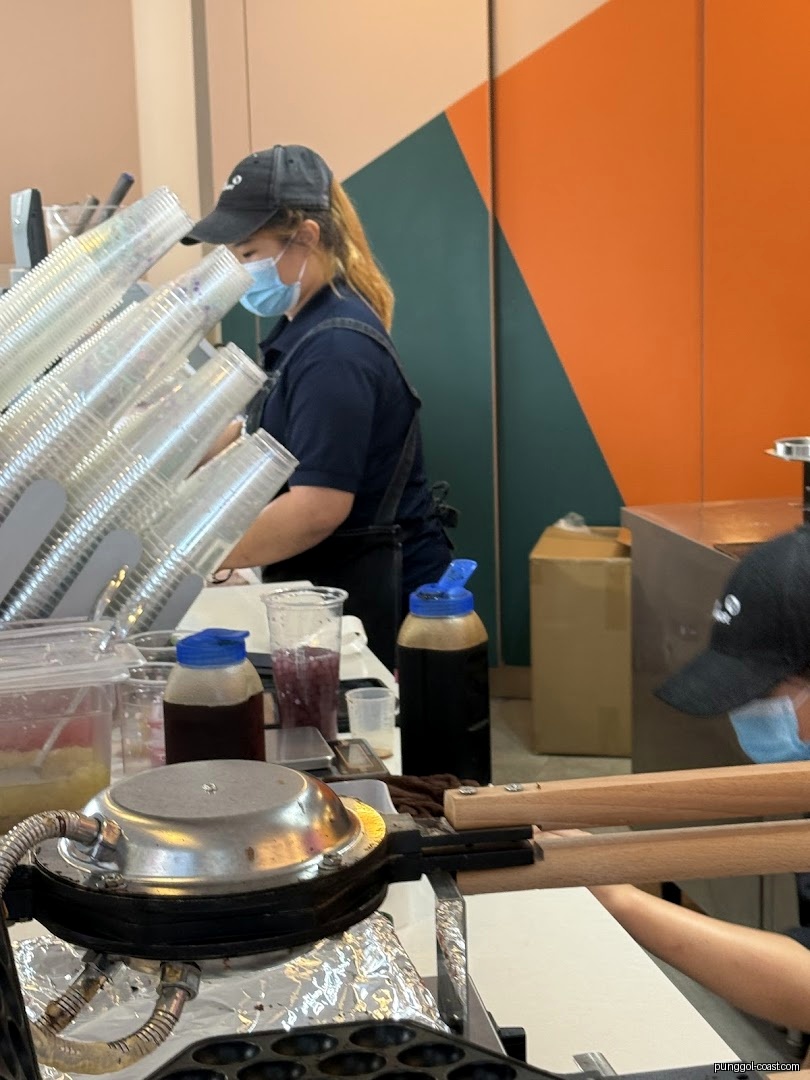 Shop staff preparing items at a counter with a waffle maker.