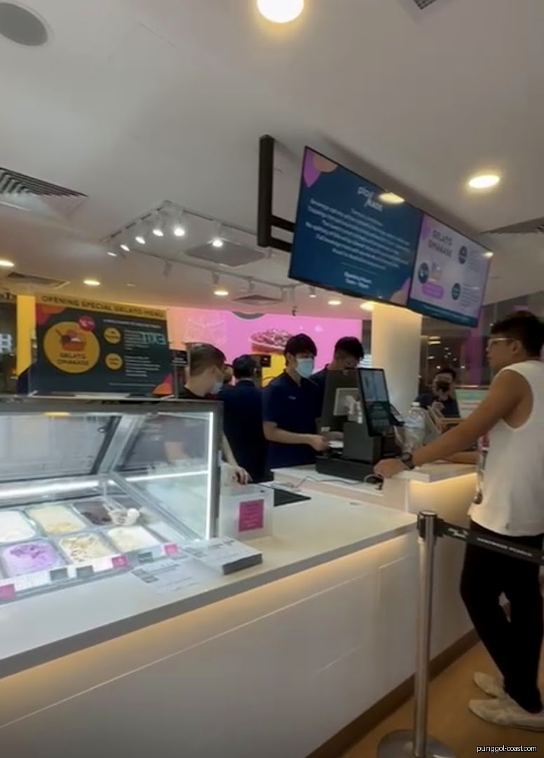 Interior of a gelato shop with staff, customer, and display counter.