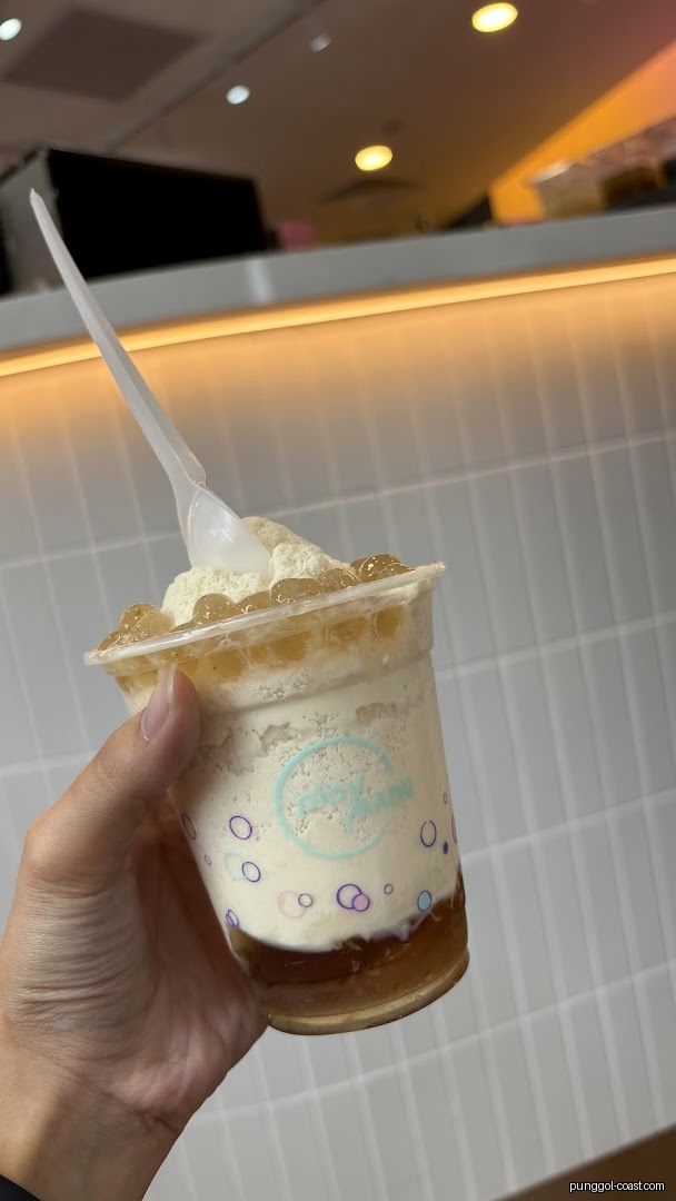 Hand holding a layered drink with toppings and a spoon.