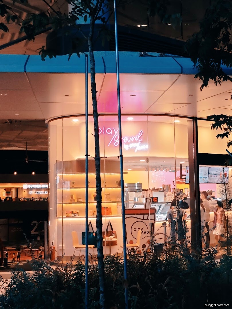 Illuminated shop front with neon sign, showing interior and people at night.