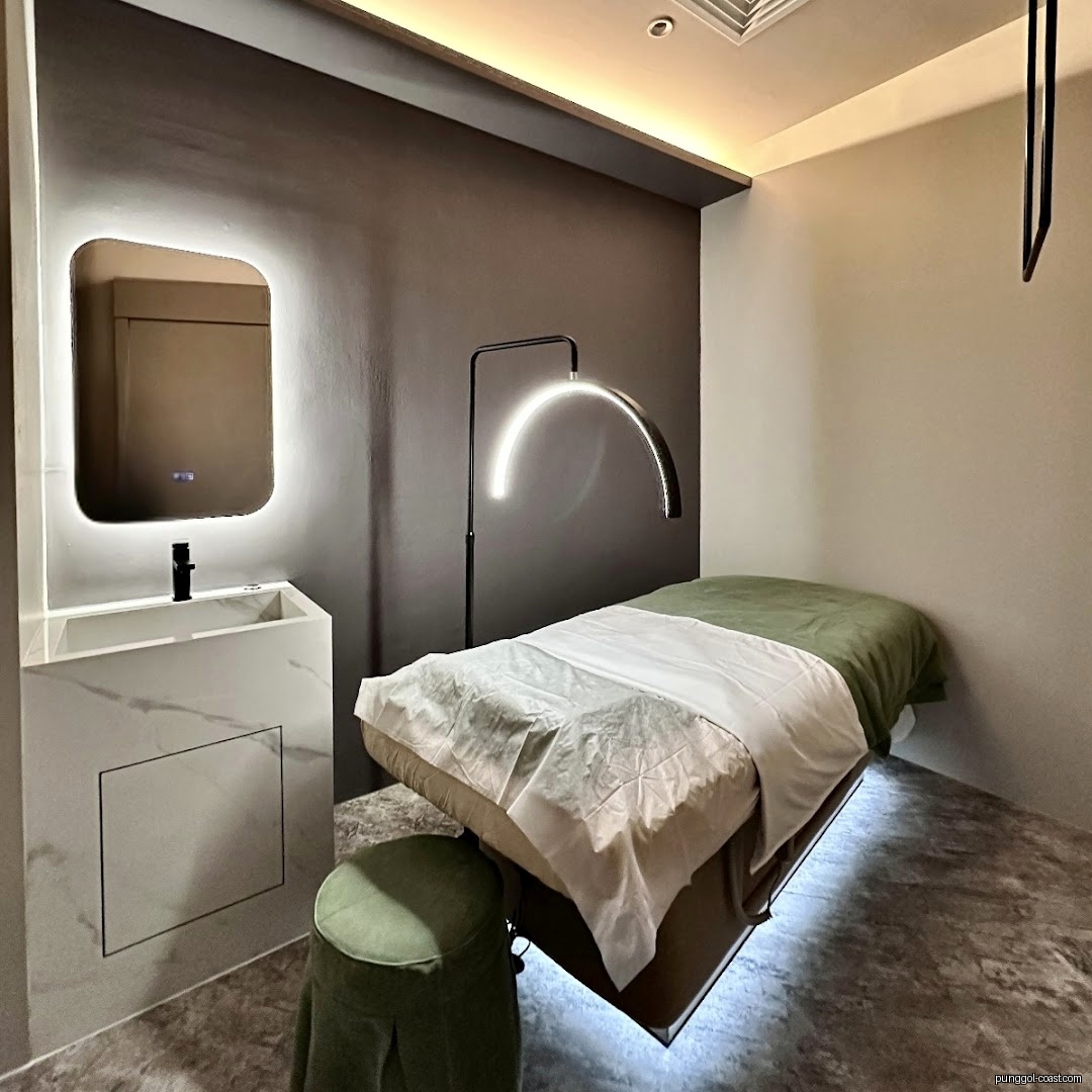 Modern treatment room with bed, specialized lamp, sink, and mirror.