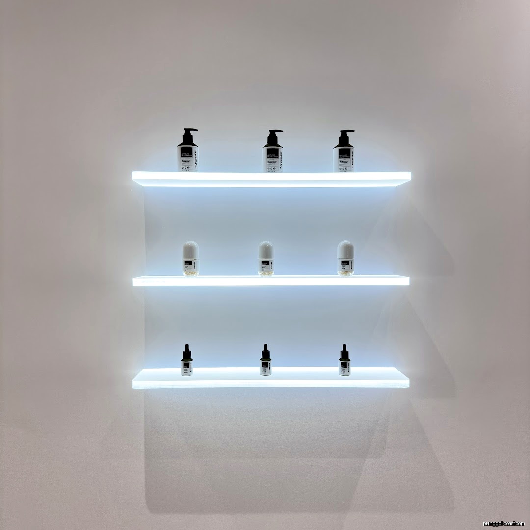 Three illuminated shelves display skincare products on a white wall.