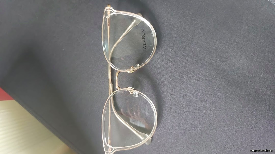 A pair of clear-framed eyeglasses with gold temples on a dark surface.
