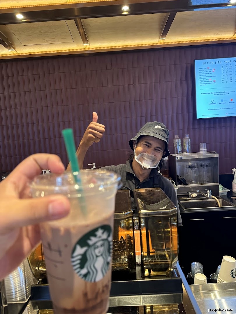 Customer holds Starbucks drink, staff gives thumbs up behind counter.