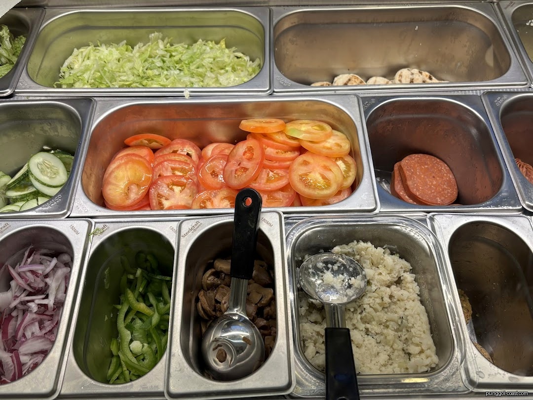 Close-up of fresh ingredients in metal trays at a Subway counter.
