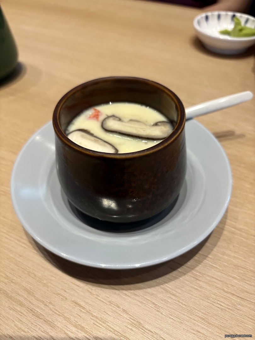 A cup of chawanmushi with mushrooms and crab stick on a table.