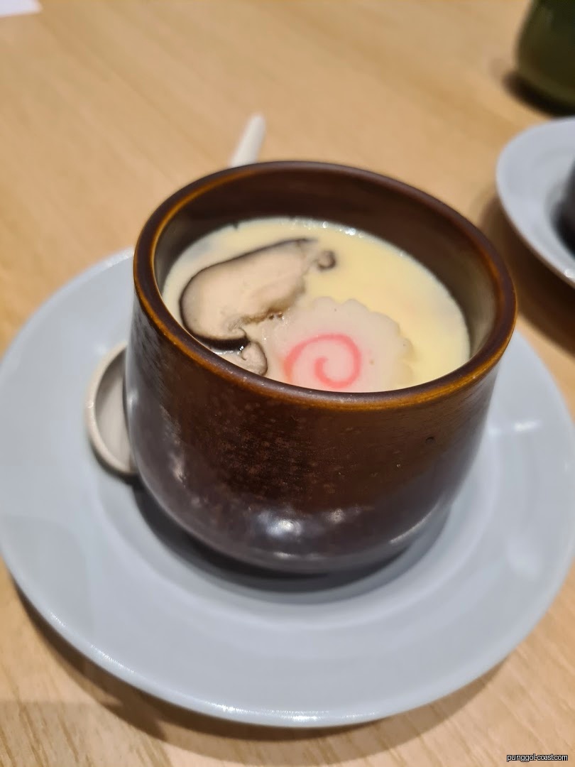 A close-up of Chawanmushi with mushroom and narutomaki in a brown cup.