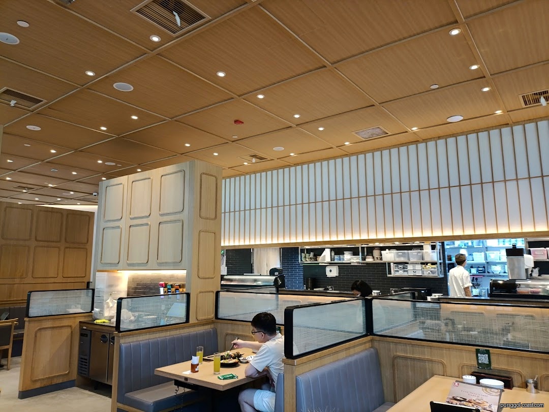 A customer dines inside a modern Sushi Tei restaurant with an open kitchen.