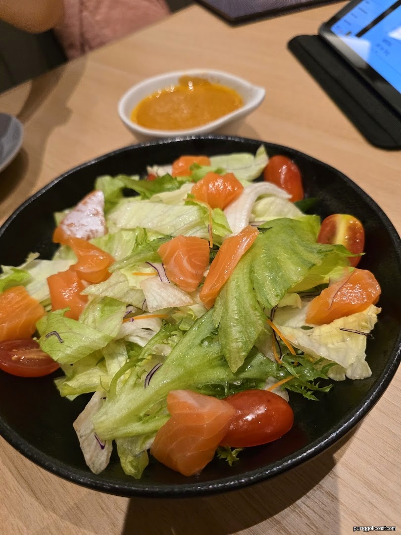 A bowl of salmon salad with cherry tomatoes and dressing on a table.