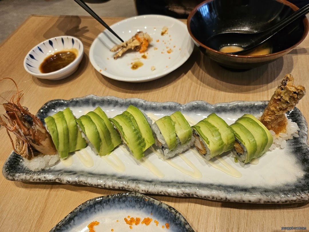 Sushi rolls with avocado, fried shrimp, and other dishes on a table.