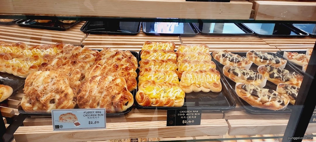 Close-up of various buns and bread displayed in a bakery's glass case.