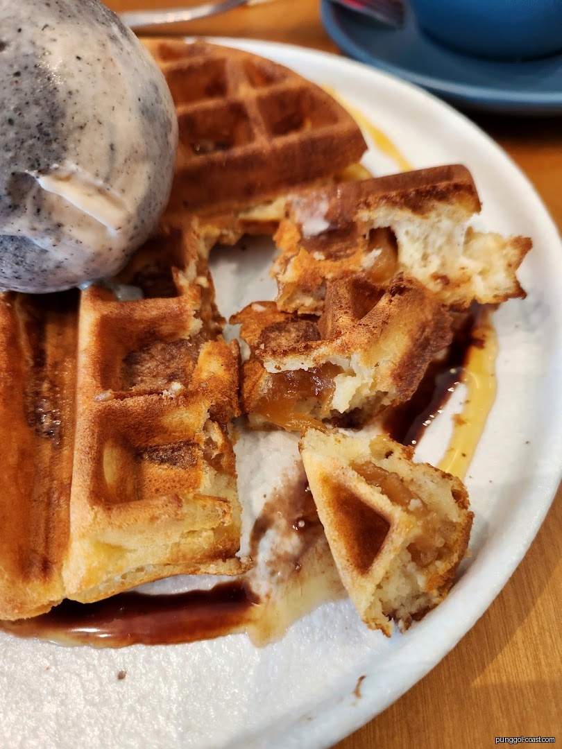 Close-up of waffles with ice cream and sauce on a white plate.