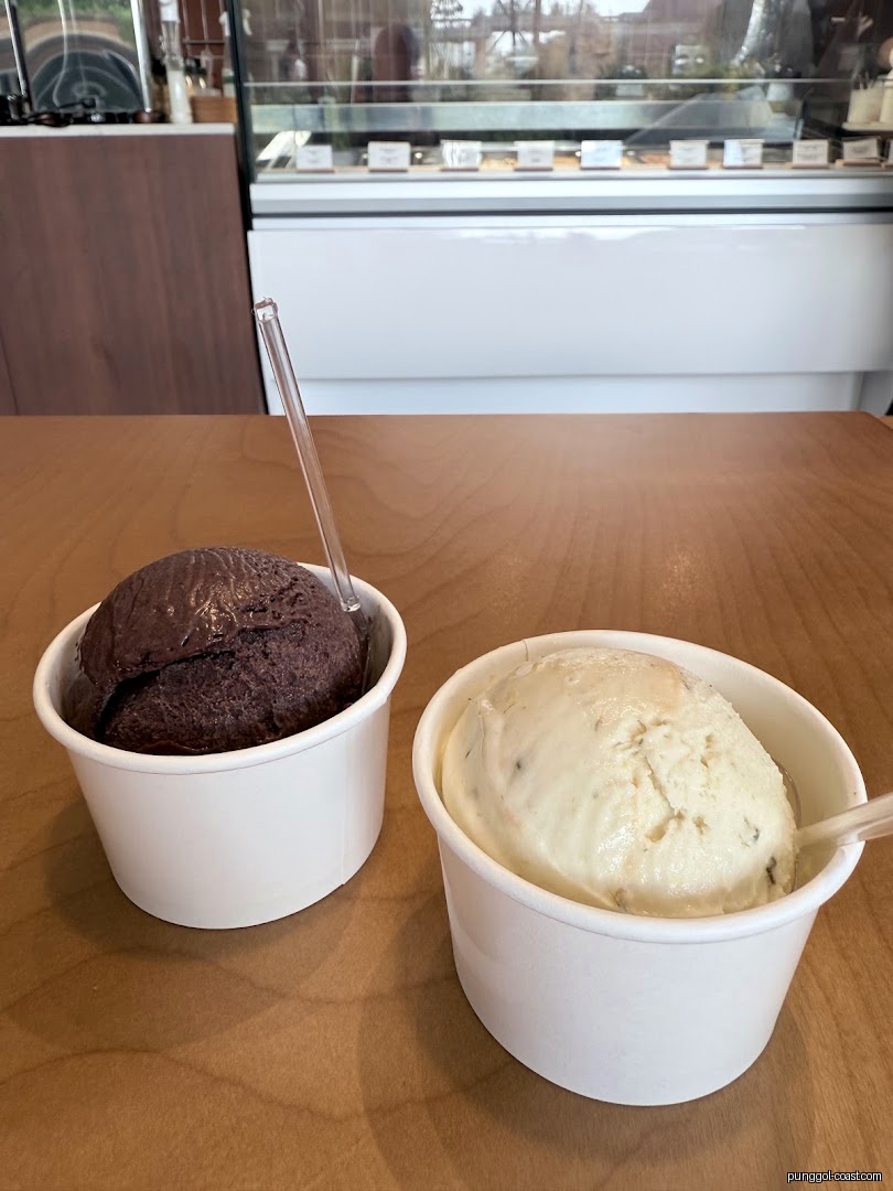 Two ice cream cups on a wooden table inside a shop.
