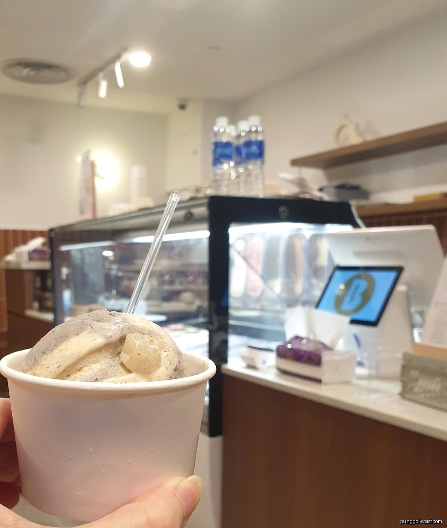 Hand holding ice cream cup inside a shop with display case.