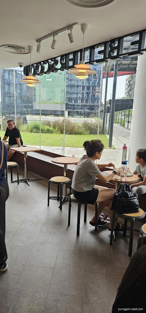 People seated inside a shop with large windows overlooking greenery.