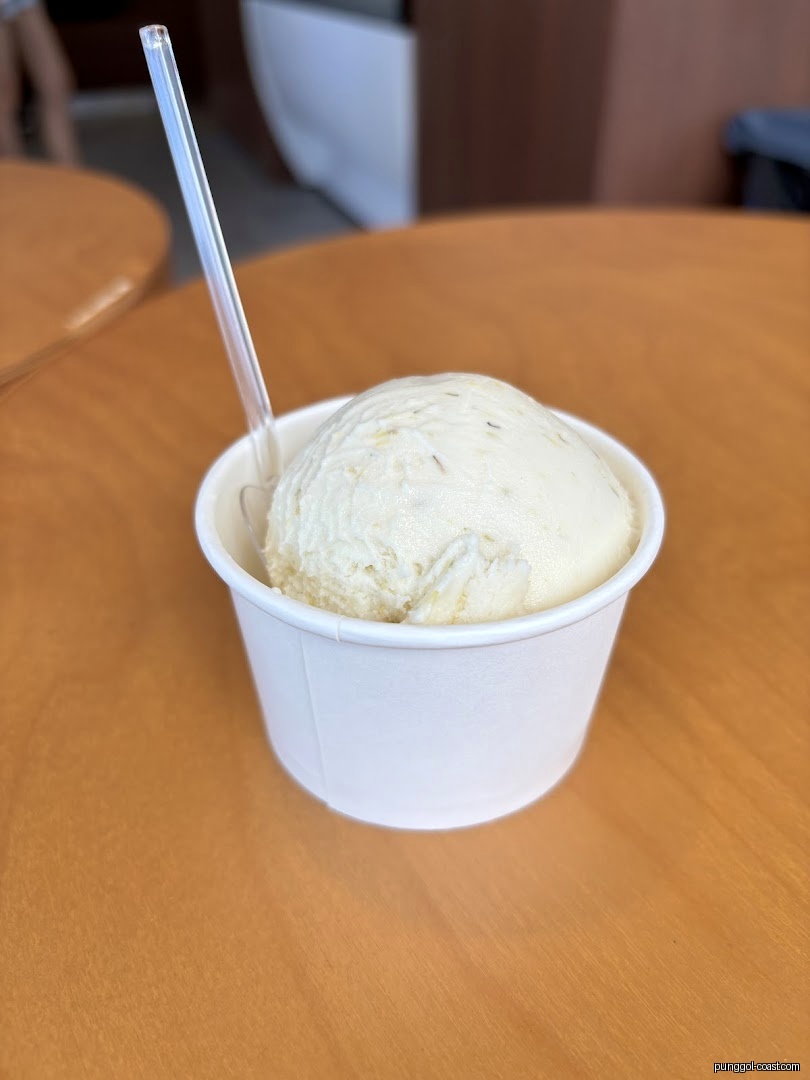 A white cup of ice cream with a spoon on a wooden table.