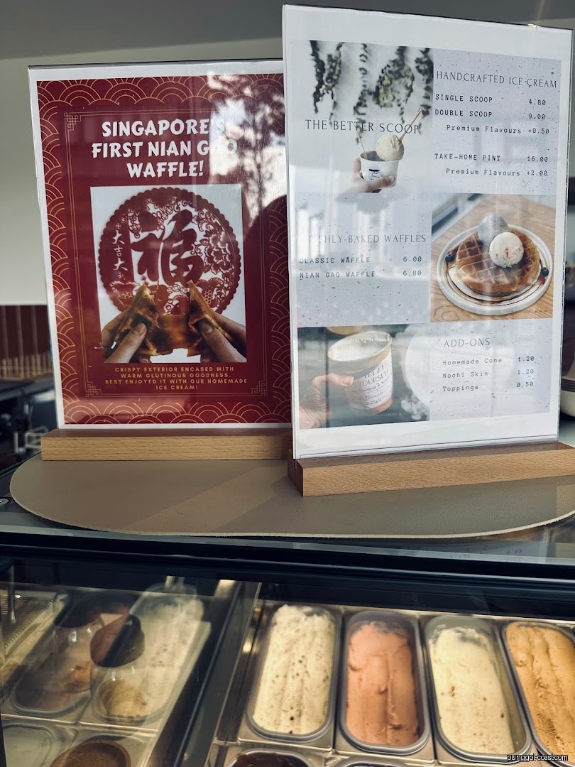 Menu and advertisement displays above ice cream tubs at a shop counter.