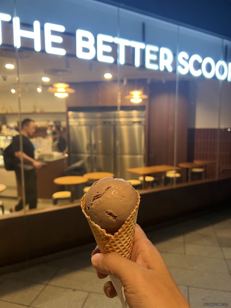 Hand holding ice cream cone in front of 'The Better Scoop' shop.